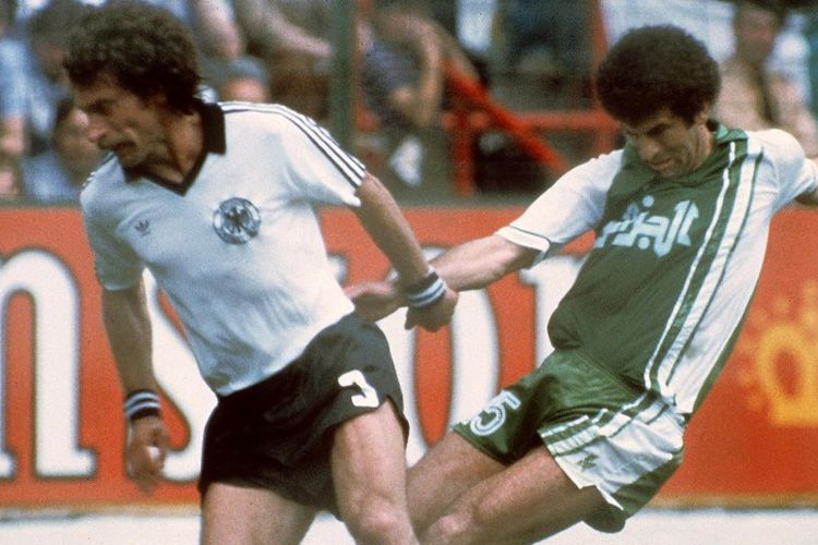 Pemain belakang Jerman Barat, Paul Breitner (kiri), berebut bola dengan gelandang Aljazair, Mustapha Dahleb dalam putaran pertama Piala Dunia 1982. Aljazair tersingkir menyakitkan dari Piala Dunia 1982 karena konspirasi Jerman dan Austria yang kemudian disebut sebagai Disgrace of Gijon. 