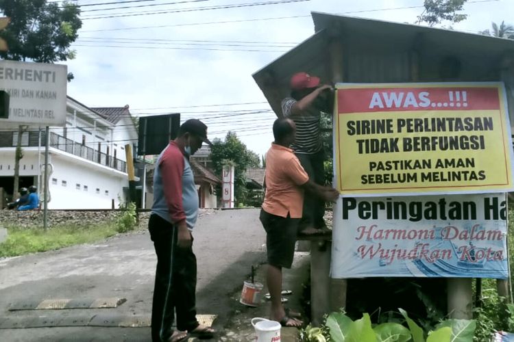 Warga memasang banner berisi pemberitahuan bahwa lampu dan sirine peringatan yang ada di perlintasan kereta api tanpa palang pintu tidak berfungsi, Minggu (13/2/2022)