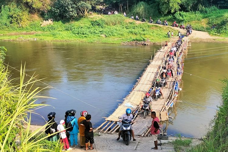 Ratusan warga Kota Solo dan Sukoharjo mengantre menyebrangi Sungai Bengawan Solo, dengan Jembatan Sasak Bambu di Sungai Bengawan Solo, Jawa Tengah. Jembatan Sasak Bambu ini dilewati para warga sejak pukul 09.00 WIB, Senin (26/9/2022). Kemudian, pada pukul 15.00 WIB, mulai terlihat kepadatan dan antrean yang mengular sejauh 1 kilometer.