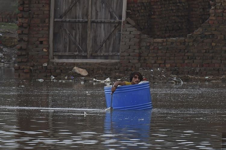 Seorang pria menggunakan drum plastik untuk menyeberangi daerah banjir setelah hujan muson lebat di Jacobabad, provinsi Sindh, pada 26 Agustus 2022. 