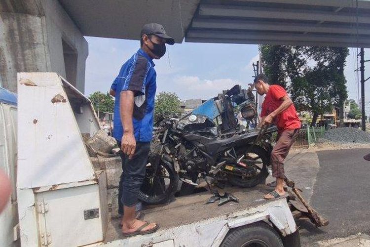 Sejumlah petugas mengangkut motor sport yang ringsek usai ditabrak kereta bandara di pintu perlintasan rel kereta di Pesing, Grogol Petamburan, Jakarta Barat pada Selasa (16/8/2022). 
