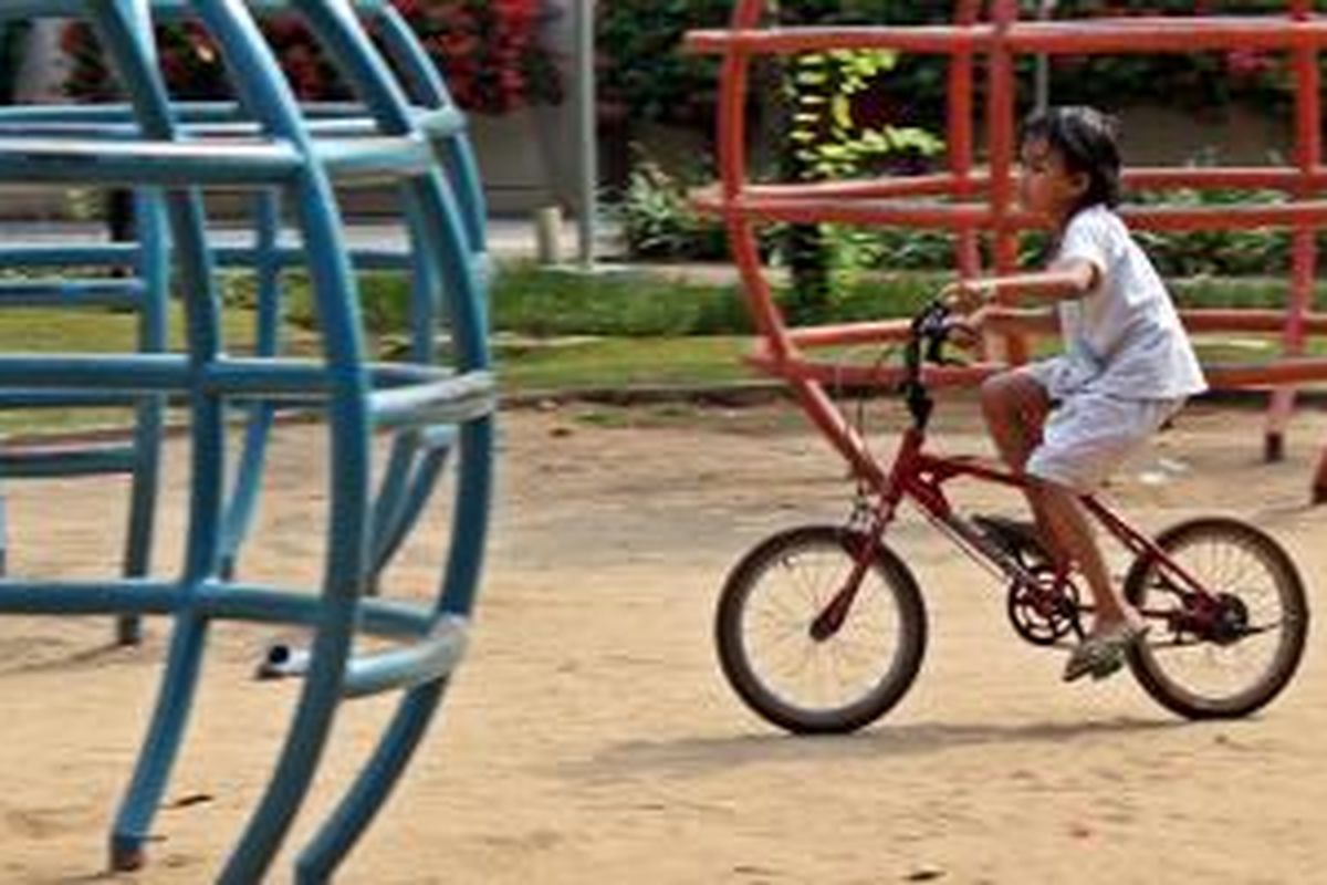 Seorang anak perempuan tengah asyik mengayuh sepedanya berputar mengelilingi Taman Menteng, Jakarta Pusat.