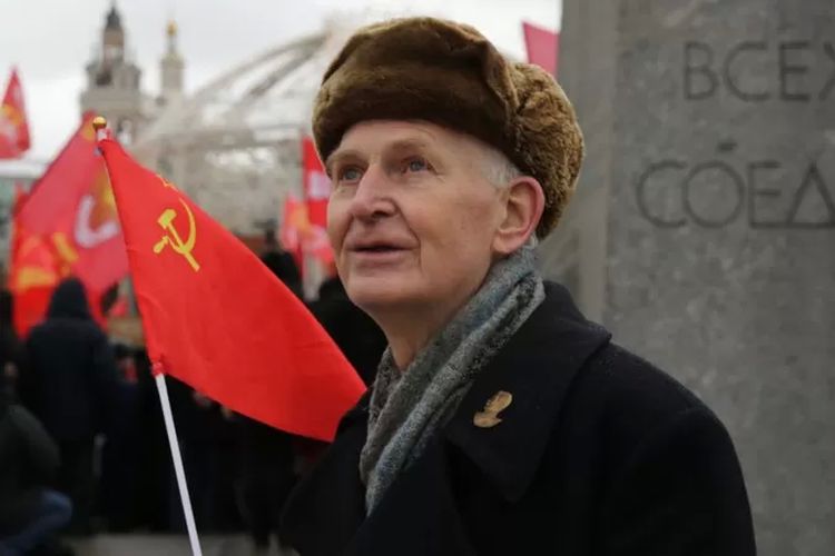Seorang lelaki tua memegang bendera Uni Soviet

