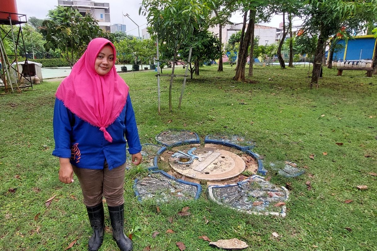 Pengelola RPTRA Kembangan, Opiani (36) berpose di depan sebuah sumur resapan yang didesain cantik berbentuk bunga, senada dengan taman bermain anak di sekitarnya, Selasa (8/11/2022).