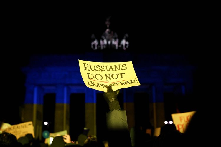 Seorang warga membawa poster di depan Brandenburg Gate yang menyala dengan lampu warna bendera Ukraina saat protes anti perang, setelah Rusia meluncurkan operasi militer besar terhadap Ukraina, di Berlin, Jerman, Kamis (24/2/2022). ANTARA FOTO/REUTERS/Christian Mang
