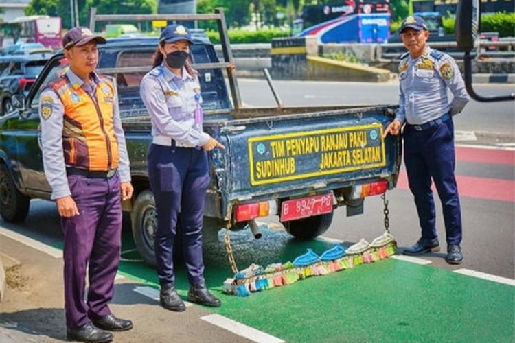 Petugas gabungan dari Suku Dinas Perhubungan dan Satuan Polisi Pamong Praja (Satpol PP) Jakarta Selatan melakukan pembersihan ranjau paku di Jalan Jenderal Gatot Subroto, Kecamatan Mampang Prapatan. 