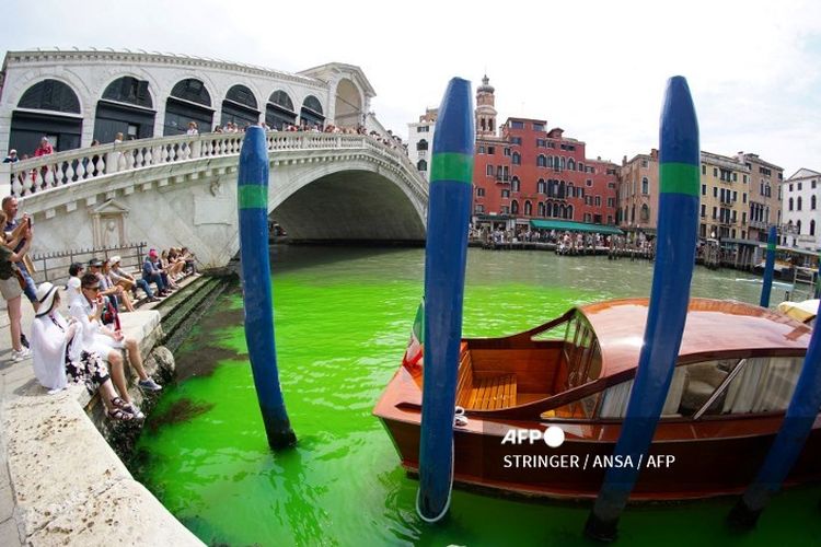 Foto, yang diambil pada Minggu (28/5/2023) oleh kantor berita Italia Ansa, menunjukan perairan berwarna hijau menyala di bawah Jembatan Rialto di Grand Canal di Venesia, Italia. Pertemuan darurat pun digelar pada Minggu (28/5/2023) guna membahas fenomena ini, khususnya terkait asal cairan tersebut.