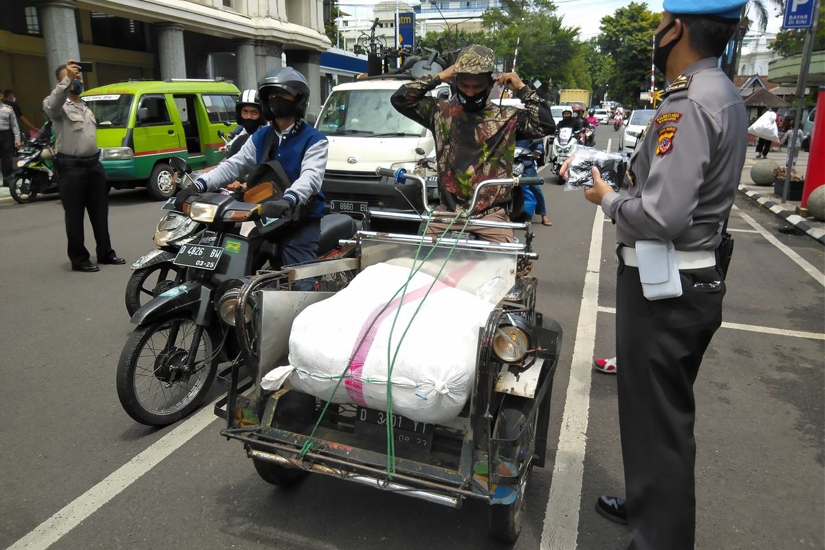 Polisi tengah membagikan masker kepada pengendara dan warga sekitar sekaligus menyosialisasikan PPKM berbasis mikro.