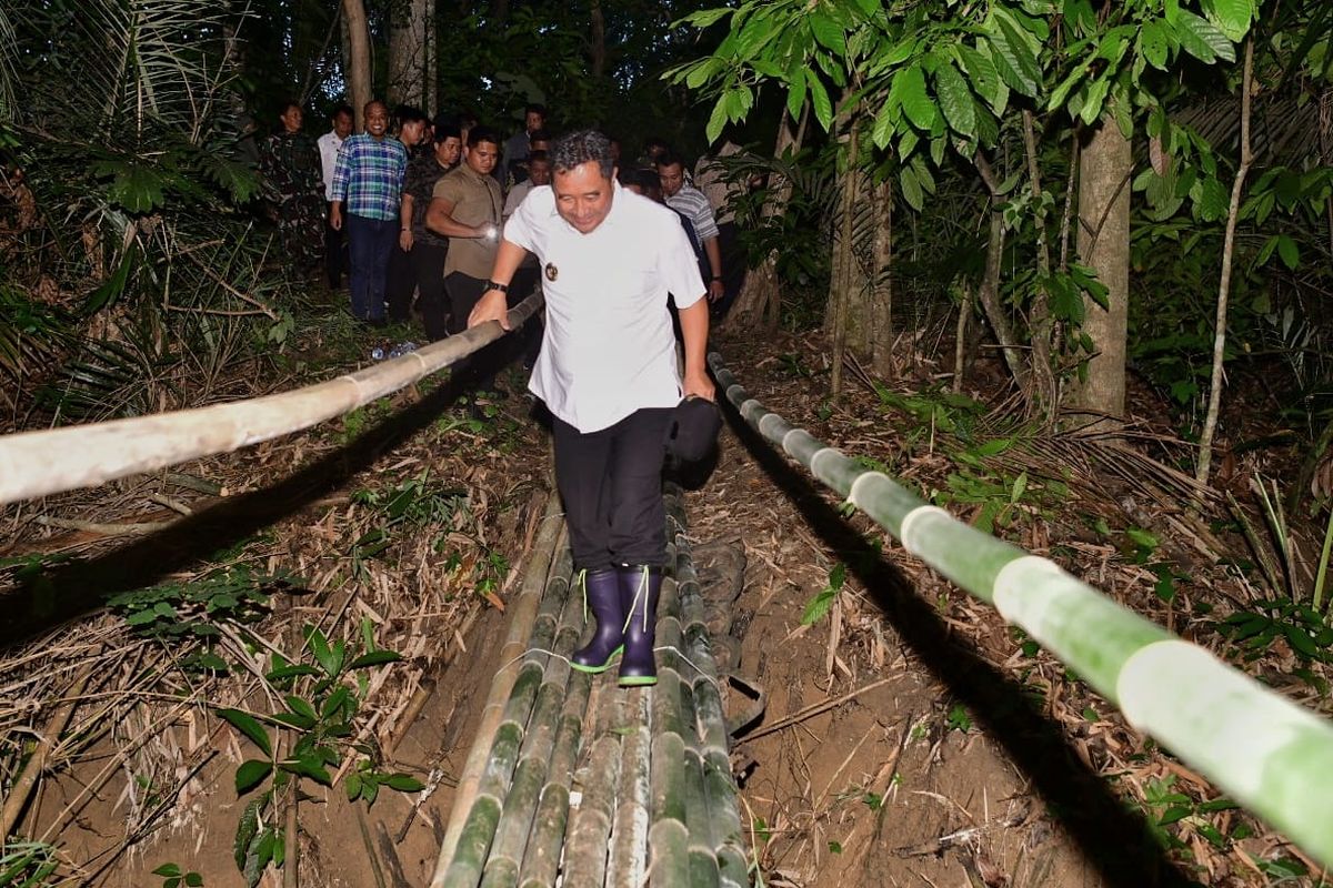 Penjabat (Pj) Gubernur Sulawesi Selatan (Sulsel) Bahtiar Baharuddin saat melewati titian dari bambu untuk melakukan penanaman budi daya pisang Cavendish di Desa Ulaweng Riaja, Kecamatan Amali, Kabupaten Bone, Kamis (12/1/2024).  
