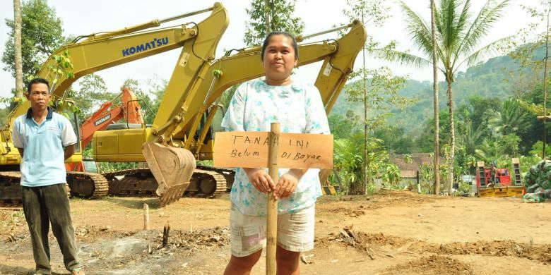 Pemilik tanah dan kandang ayam, Winarni (40) didesa Watuagung, Tuntang, Kabupaten Semarang memegang papan protes dengan latar belakang alat berat.