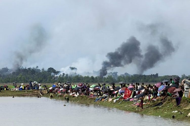 Asap hitam mengepul di banyak tempat di sebuah desa di negara bagian Rakhine, Myanmar, yang diyakini ada pembakaran rumah-rumah warga Rohingya. Warga korban pun hanya memandang sedih
