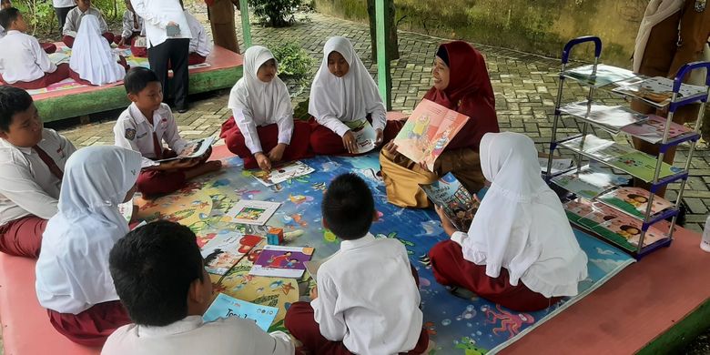 Aktivitas membaca buku bersama antara guru dan murid di SDN 005 Makmur di Kabupaten Pelalawan, Provinsi Riau. 
