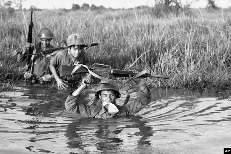 Seorang tentara Vietnam Selatan memegang barang-barang pribadinya di dalam kantong plastik di antara giginya saat unitnya melintasi sungai Delta Mekong yang berlumpur di Vietnam dekat perbatasan Kamboja, 11 Maret 1972.
