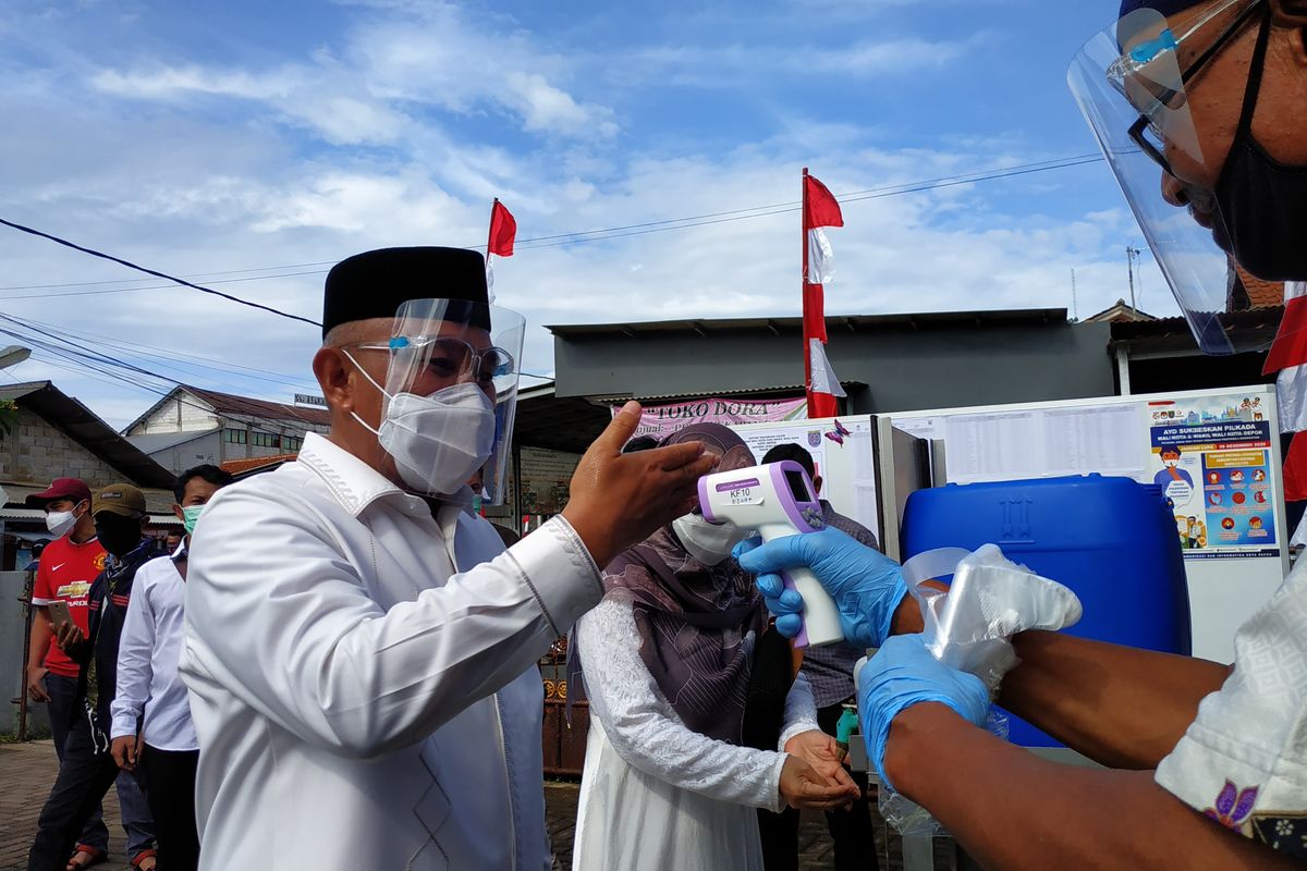 Calon wali kota Depok petahana, Mohammad Idris diperiksa suhu tubuhnya di punggung tangan ketika hendak mencoblos di TPS 14 Jatimulya, Cilodong, Rani (9/12/2020).