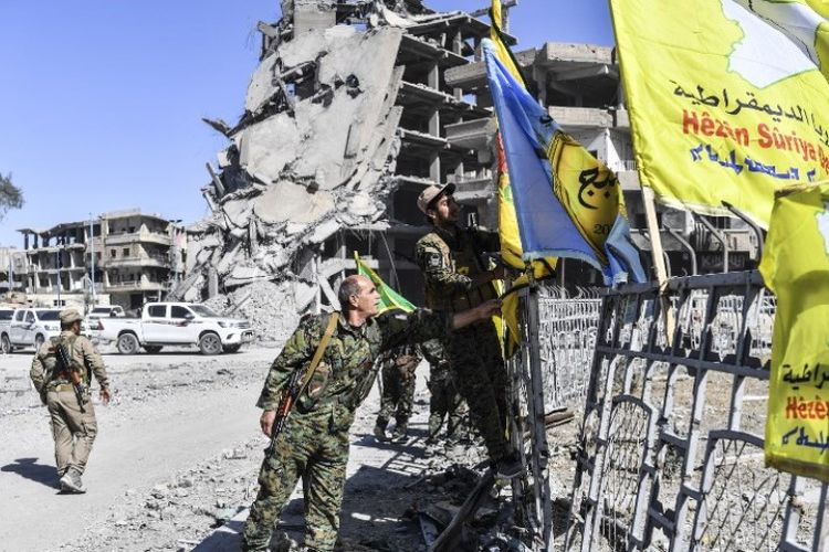 Seorang prajurit SDF mengibarkan bendera pasukannya di bundaran Al-Naim di kota Raqqa yang direbut dari tangan ISIS pada Selasa (17/20/2017).