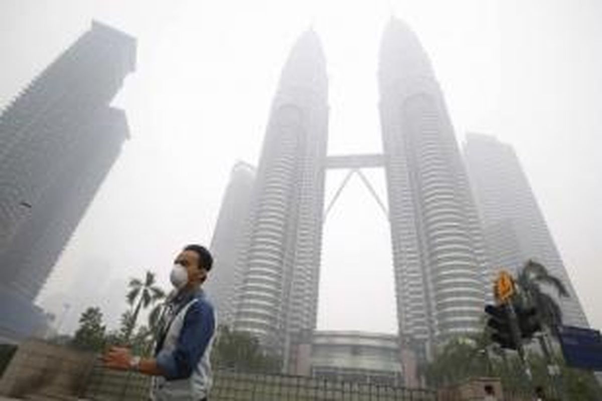 Seorang pria mengenakan masker ketika melintas di dekat Petronas Twin Towers yang tengah disellimuti kabut asap di Kuala Lumpur, Malaysia, 14 September 2015. Kabut asap berasal dari kebakaran hutan dan lahan di Sumatera, Indonesia.