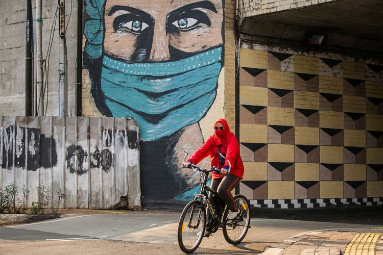 Warga menggunakan sepeda saat melintasi mural berisi pesan ajakan menggunakan masker di Cikoko, Pancoran, Jakarta Selatan, Sabtu (3/10/2020). Pembatasan sosial berskala besar (PSBB) di Jakarta untuk mengendalikan penularan Covid-19 telah memasuki pekan ketiga.