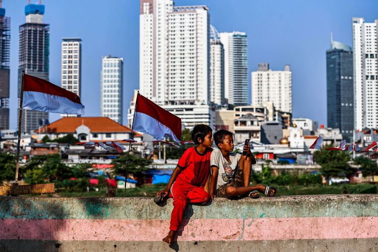 Anak-anak tampak menggunakan gawai saat temannya bermain sepakbola di taman samping Banjir Kanal Barat (BKB) di kawasan Petamburan, Jakarta Pusat, Senin (17/8/2020). Di hari Kemerdekaan Republik Indonesia ke-57 ini, anak-anak di kawasan Petamburan tetap melakukan permainan untuk menyemarakkan kemerdekaan ini.