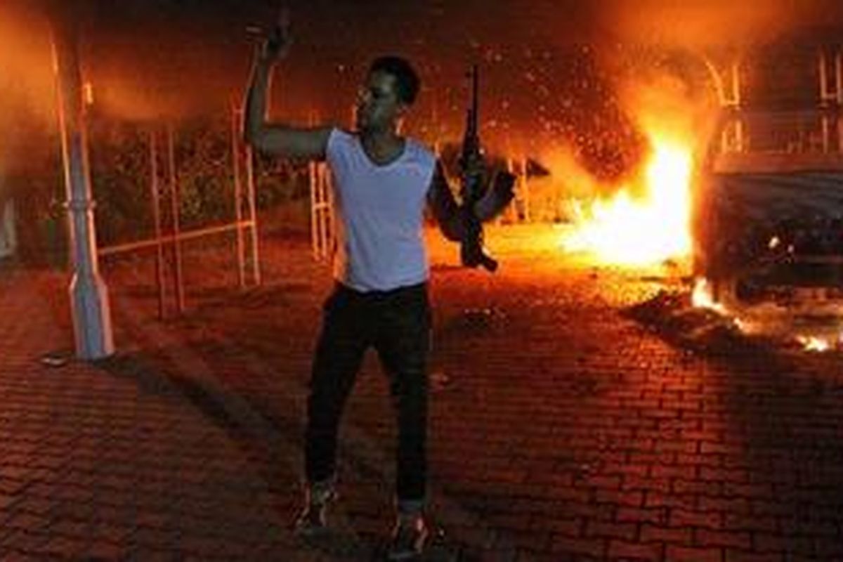 Seorang penyerbu mengacungkan senjatanya di depan sebuah mobil yang terbakar di dekat Konsulat AS di Benghazi, Libya.