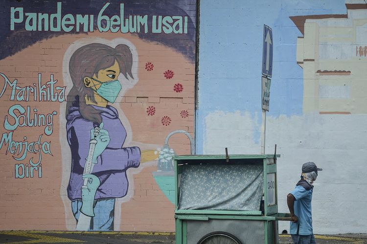 Seorang pedagang menarik gerobaknya dengan latar belakang mural imbauan 'Pandemi Belum Usai di Jakarta, Minggu (18/7/2021). ANTARA FOTO/M Risyal Hidayat/foc.