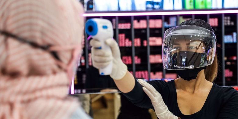 Pekerja salon menggunakan masker dan pelindung wajah, melakukan pemeriksaan suhu tubuh menggunakan thermo gun saat melayani pelanggan.