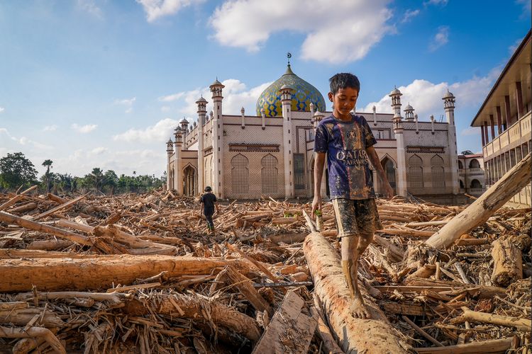 Seorang bocah berjalan meniti kayu-kayu yang memenuhi area Pondok Pesantren Darul Mukhlishin pascabanjir bandang di  Desa Tanjung Karang, Karang Baru, Kabupaten Aceh Tamiang, Aceh, Jumat (5/12/2025). Usai sepekan setelah bencana banjir bandang, akses menuju Desa Tanjung Karang masih terhambat akibat banyaknya tumpukan pohon dan lumpur tebal dari Sungai Tamiang sehingga bantuan sulit masuk ke wilayah tersebut. ANTARA FOTO/Erlangga Bregas Prakoso/app/foc.