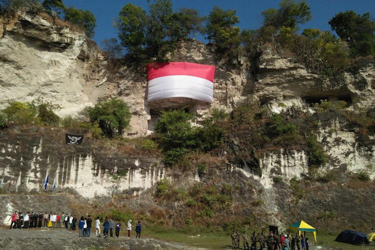 Pemuda dan warga melaksanakan upacara bendera memperingati HUT RI ke-76 di bawah bentangan bendera raksasa di Bukit Kapur, Desa Suci, Kecamatan Manyar, Gresik, Selasa (17/8/2021).
