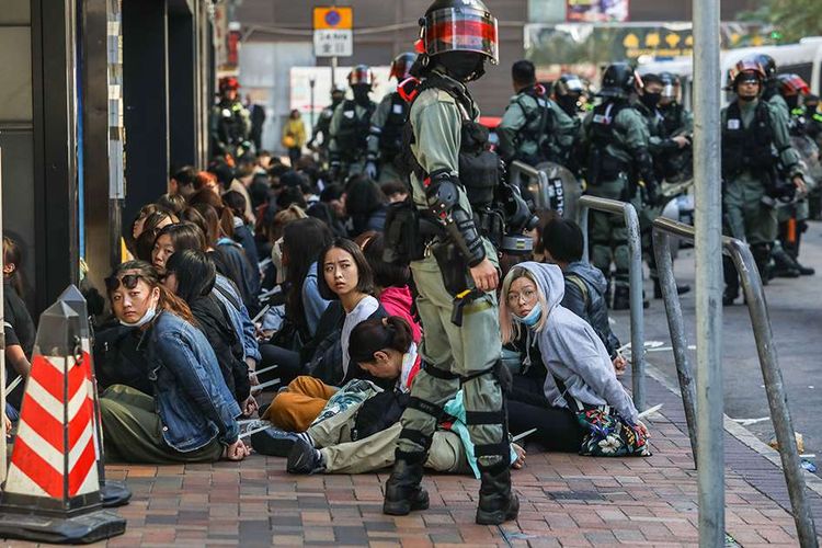 Orang-orang ditahan oleh polisi di dekat Universitas Politeknik Hong Kong di distrik Hung Hom, Hong Kong, Senin (18/11/2019). Kericuhan bermula dari aksi pendemo menduduki kampus selama beberapa hari hingga berujung aksi lempar dan bentrokan dengan polisi.