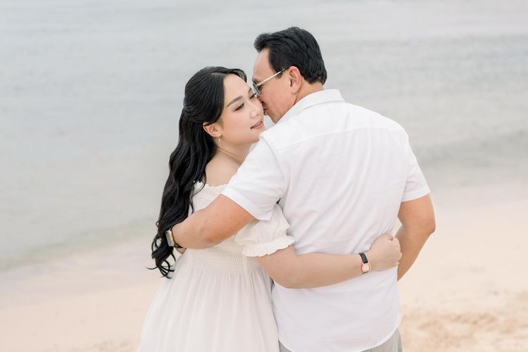 Puput Nastiti Devi tampil anggun dengan long dress putih, makeup natural, dan rambut wavy saat foto kehamilan anak ketiga bersama keluarga.
