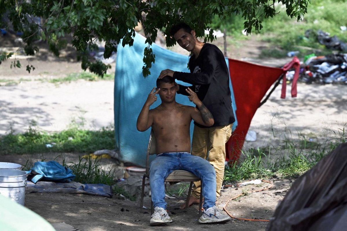 Seorang pria migran melambaikan tangan ke kamera sambil memotong rambutnya di kamp darurat di tepi Rio Grande di Matamoros, Negara Bagian Tamaulupas, Meksiko pada 9 Mei 2023. Gelombang migran diperkirakan terjadi di kota-kota perbatasan AS-Meksiko karena pemerintahan Presiden Biden secara resmi mengakhiri penggunaan Title 42. Pada 11 Mei, pemerintahan Presiden Joe Biden akan mencabut Title 42, protokol ketat yang diterapkan oleh presiden sebelumnya Donald Trump untuk menolak masuknya migran dan mengusir pencari suaka berdasarkan darurat pandemi Covid-19.