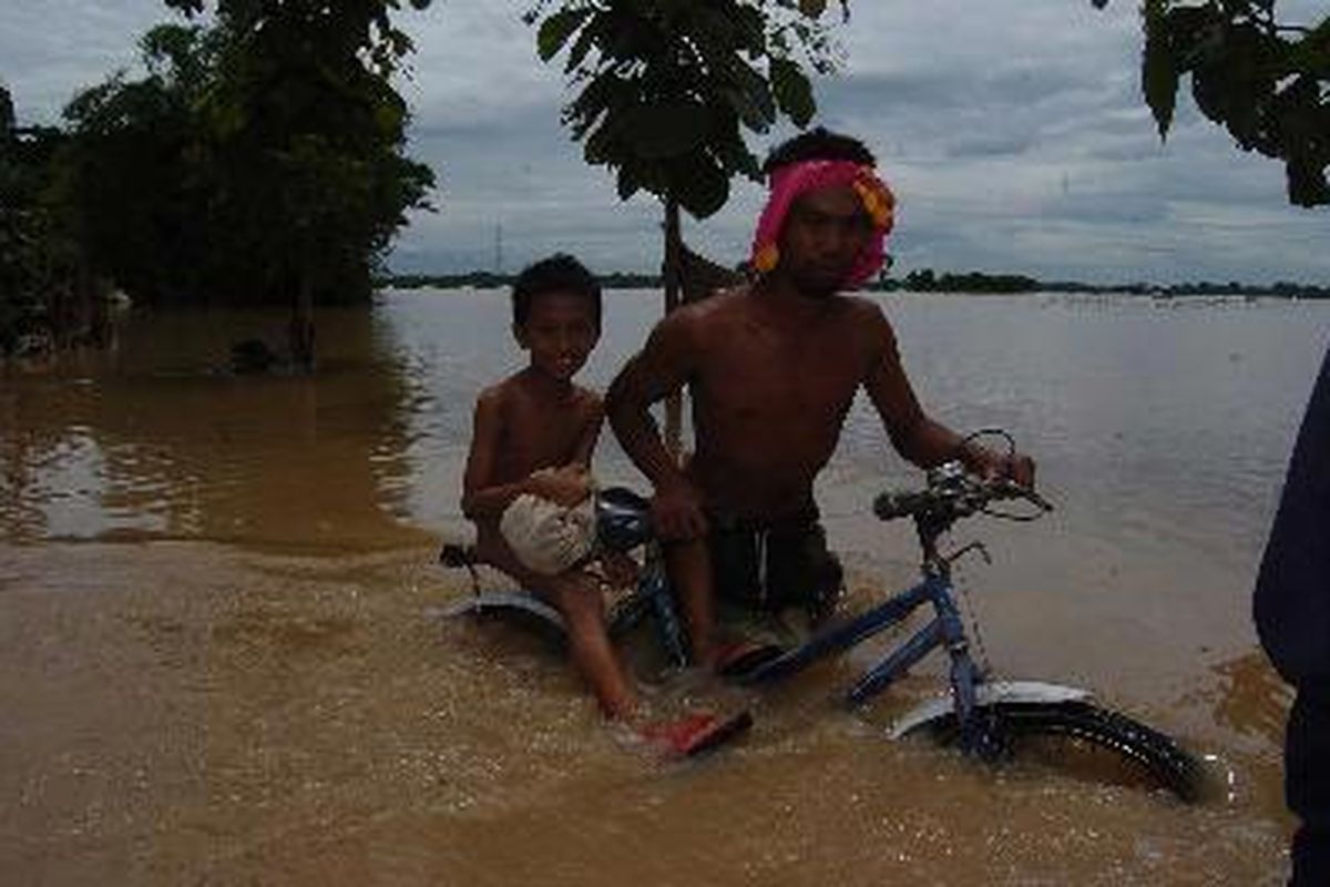 Lintasi Banjir - Seorang warga Desa Gunting Kecamatan Geneng bersama anaknya, melintasi banjir yang menggenangi desa mereka, Sabtu (29/12). Kini sejumlah warga desa mulai mengusungi benda-benda mereka yang masih tersisa ketempat yang aman.