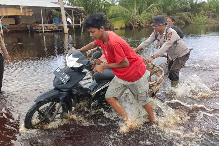 Petugas kepolisian mengevakuasi salah satu pengendara sepeda motor yang mogok di jalan lintas timur sumatera yang terendam banjir, di Desa Kemang, Kecamatan Pangkalan Kuras, Kabupaten Pelalawan, Riau, Sabtu (27/1/2024).