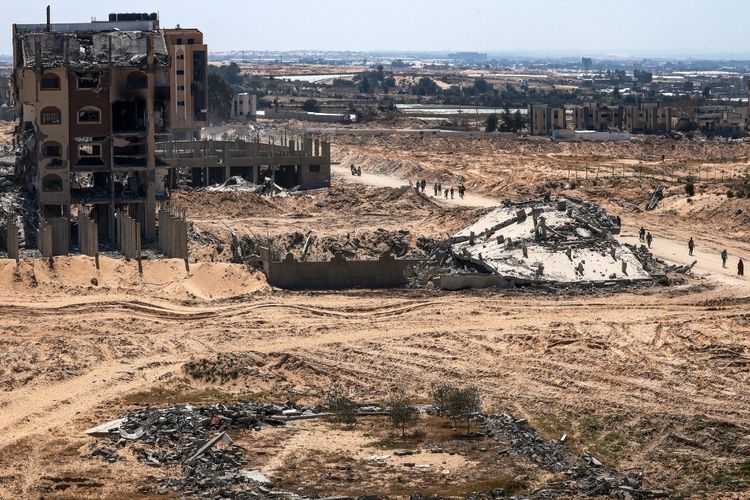 Orang-orang berjalan melewati bangunan yang rusak dan hancur di Khan Yunis pada 7 April 2024, setelah Israel menarik pasukan daratnya keluar dari Jalur Gaza selatan, Minggu (7/4/2024) hari ini.