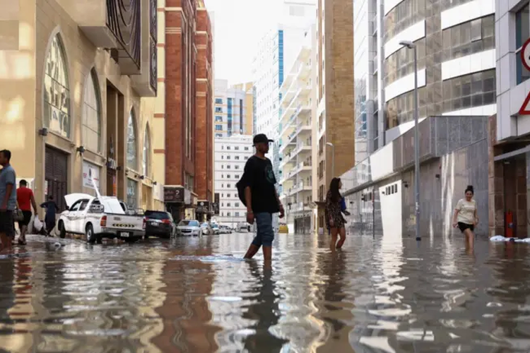 Orang-orang berjalan melintasi genangan banjir yang terjadi akibat hujan lebat, di Dubai, Uni Emirat Arab, 17 April 2024.