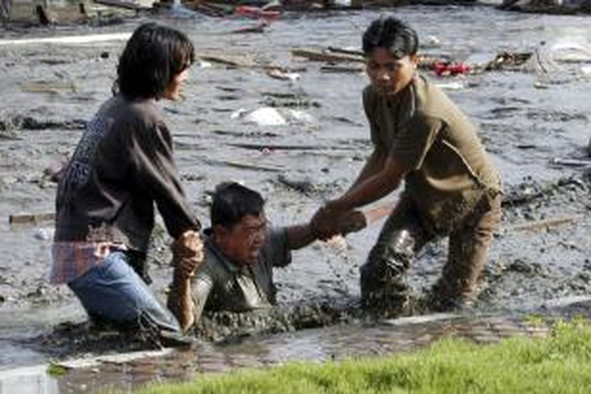 Foto yang diambil sesaat setelah tsunami mengempaskan Aceh pada 26 Desember 2004 ini memperlihatkan dua orang muda sedang berusaha menarik lelaki paruh baya dari air pekat sisa gelombang tsunami ke daratan.