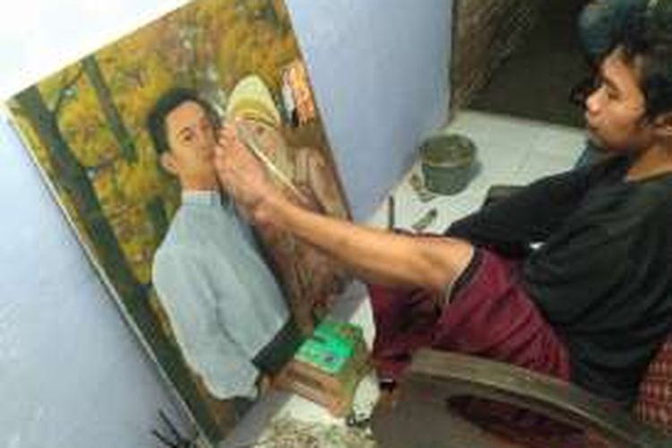 Lukman Hakim pelukis yang menggunakan kaki asal Banyuwangi saat mengerjakan lukisan pesanannya