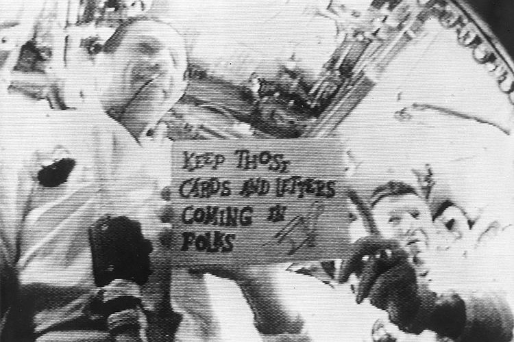 Selama siaran televisi pertama, komandan Apollo 7 Wally Schirra, kanan, menampilkan salah satu dari beberapa pesan untuk pemirsa di Bumi.
