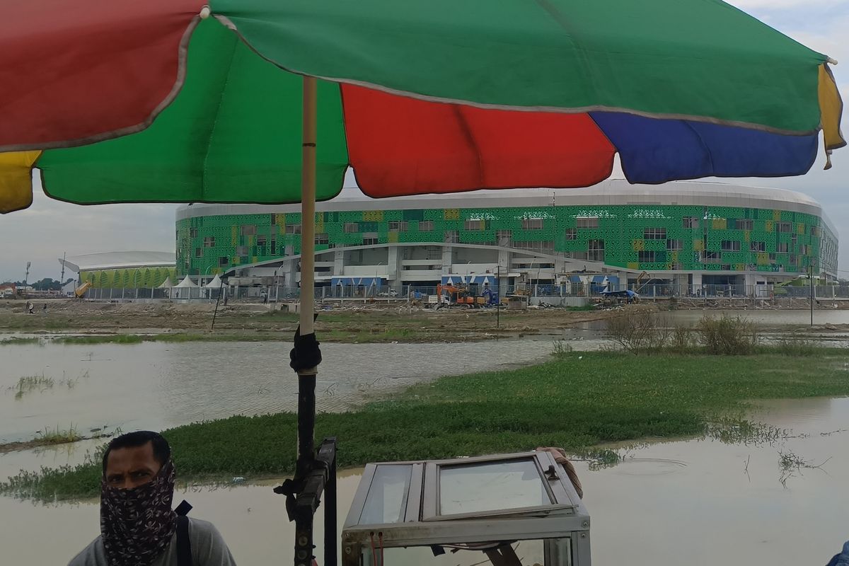Seorang pria sedang menjajakan dagangan bakso bakar dengan background Stadion Utama PON, Sport Center di Deli Serdang, Rabu (18/9/2024). Pemprov Sumut menyebut pembanguan stadion telah rampung pada Kamis (19/9/2024) dan siap digunakan untuk penutupan PON pada Jumat (20/9/2024).