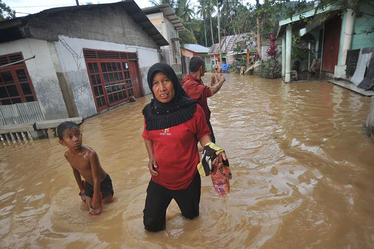 Warga melintasi banjir yang merendam pemukiman di Kampung Tarandam, Nagari Pasar Muara Labuah, Kab.Solok Selatan, Sumatera Barat, Jumat (13/12/2019). Data BPBD Solok Selatan menyebutkan banjir bandang mengakibatkan 1000 unit rumah terendam banjir, enam unit hanyut, satu jembatan putus dan satu orang tewas.