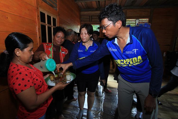 Para peserta Bersepeda di Jantung Borneo saat disuguhi tuak ketika memasuki Rumah Betang Kedungkang, Kalimantan Barat, Sabtu (28/10/2017). Perhelatan Bersepeda di Jantung Borneo diselenggarakan bertepatan dengan agenda besar Festival Danau Sentarum Betung Kerihun, memadukan olahraga dan ekowisata serta mengajak masyarakat menyadari lebih dalam arti dari konservasi.