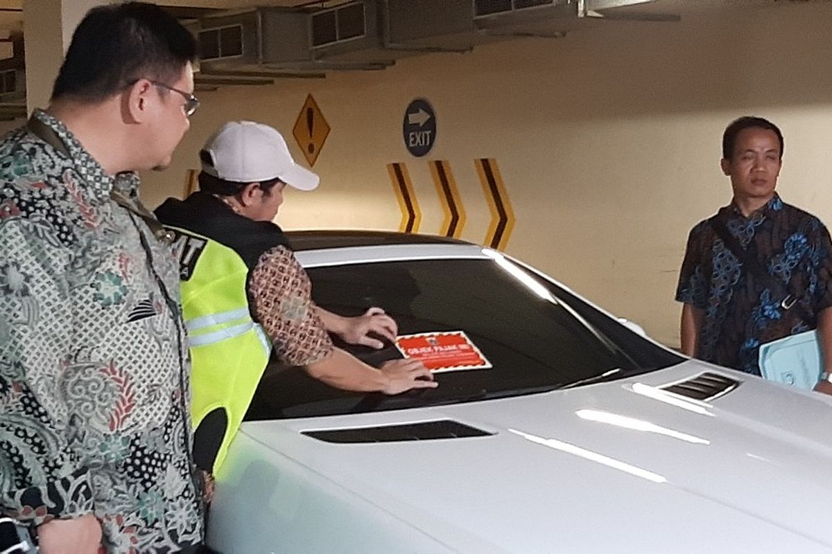 Petugas memasang stiker ke mobil yang belum dibayar pajaknya di Apartemen Regatta, Jakarta Utara, Kamis (5/4/2019).