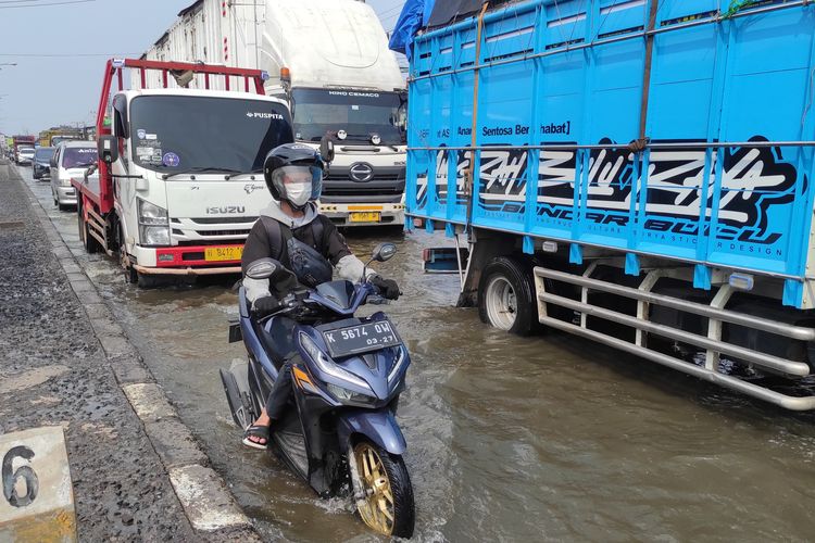 Seorang pemotor melintas di ruas jalan tepi trotoar untuk menghindari genangan air rob Pantura Demak-Semarang, Selasa (12/11/2024) pagi.