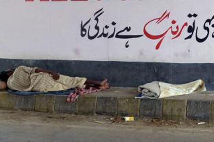 Seorang pria beristirahat di tepian jalan di kota Karachi untuk menghindari sengatan panas.