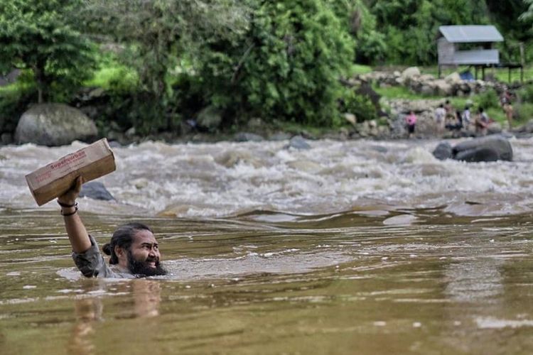 Aktor Adhin Abdul Hakim saat menyelamatkan bantuan untuk warga Pattaro, Sulawesi Selatan, yang ada di sebrang sungai. 