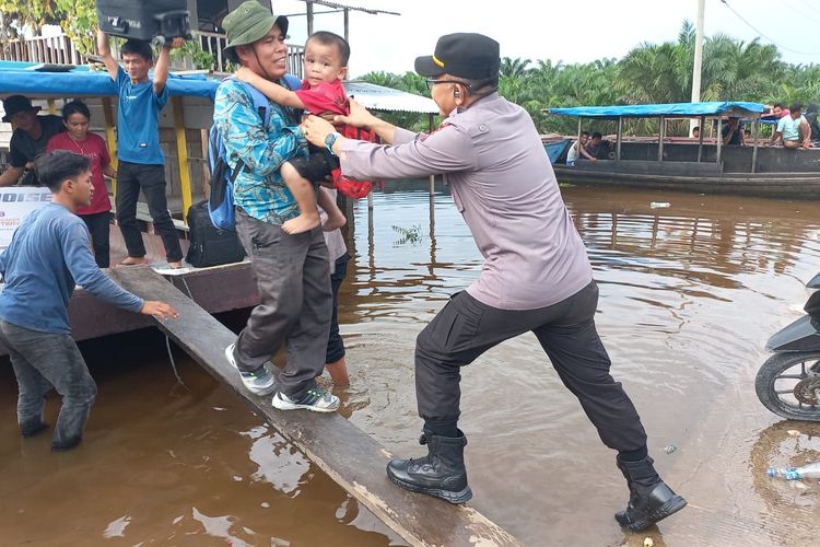 Kapolsek Pangkalan Lesung, AKP A.R Tinambunan membantu warga turun dari pompong di lokasi jalan lintas timur sumatera yang terendam banjir, di Kabupaten Pelalawan, Riau, Selasa (16/1/2024).