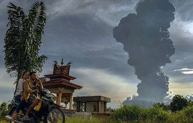 Pengendara melintas dengan latar belakang Gunung Sinabung menyemburkan material vulkanik saat erupsi, di Karo, Sumatera Utara, Minggu (9/6/2019). Gunung Sinabung berstatus Siaga (Level III) kembali mengalami erupsi dengan tinggi kolom abu mencapai 7.000 meter dan menyebabkan sejumlah desa tertutup debu vulkanik.