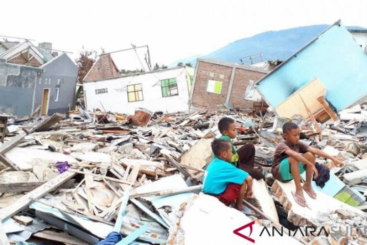 Beberapa anak sedang duduk di atas puing-puing rumah yang rusak akibat likuefaksi di atas bekas kawasan eks likuefaksi Balaroa.