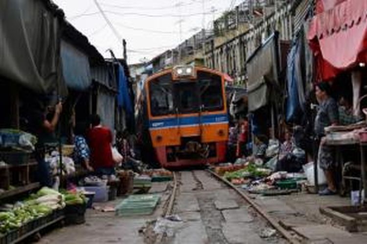 Kereta melewati pasar makanan di Maeklong, 60 kilometer Bangkok. Beberapa kali sehari, pemilik toko dengan cepat mengemas warung makanan mereka dan menarik kembali kanopi mereka untuk membiarkan kereta lewat.