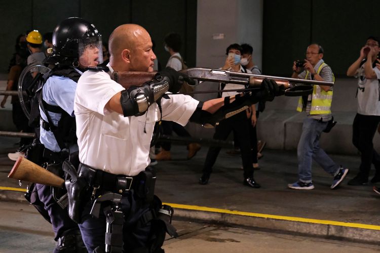 Seorang polisi mengarahkan senjata api saat bentrok dengan pengunjuk rasa anti rancangan undang-undang ekstradisi yang mengelilingi sebuah kantor polisi dimana pengunjuk rasa yang ditangkap ditahan di Hong Kong, China, Selasa (30/7/2019).