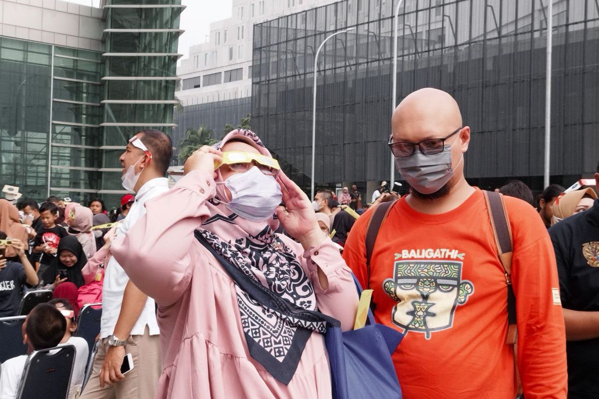 Seorang penonton tampak mencoba kacamata bantu untuk menyaksikan gerhana matahari hibrida di Taman Ismail Marzuki, Jakarta Pusat, pada Kamis (20/4/2023). (KOMPAS.com/XENA OLIVIA)